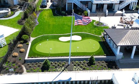 Luxurious backyard putting green, American flag, manicured lawn, waterfront property. Residential landscaping near me| Down To Earth Landscaping | Jackson New Jersey, USA (732) 833-7702