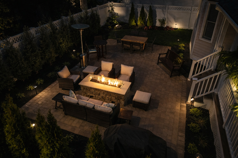 Illuminated residential patio at night with glowing fire pit and outdoor furniture.