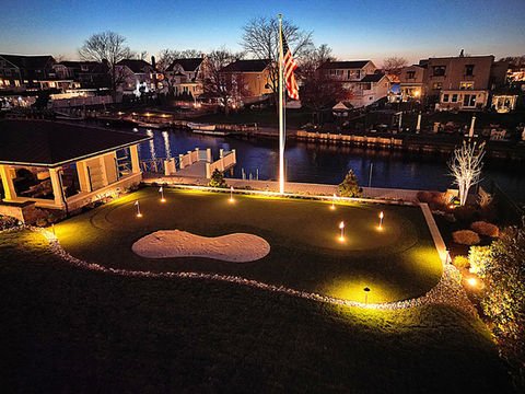 Illuminated backyard putting green, American flag, canal, and waterfront homes. Residential landscaping near me| Down To Earth Landscaping | Jackson New Jersey, USA (732) 833-7702