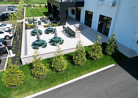 Professionally landscaped outdoor patio with green picnic tables, umbrellas, modern building, parking lot. | Down To Earth Landscaping | Jackson New Jersey, USA (732) 833-7702