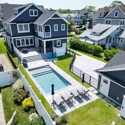 Elegant dark blue house, backyard swimming pool, patio, and green lawn.