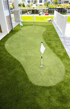 Artificial turf putting green with four flags, red golf ball, water background. Residential landscaping near me| Down To Earth Landscaping | Jackson New Jersey, USA (732) 833-7702
