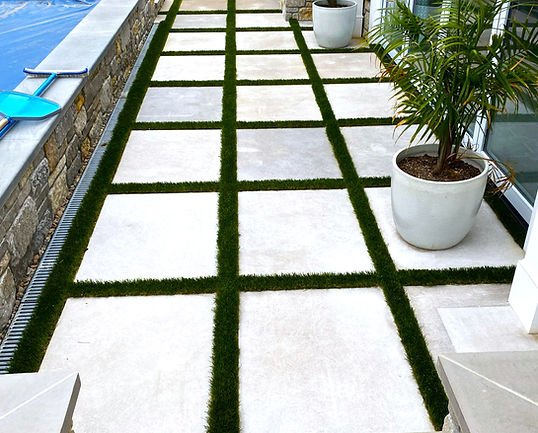 Modern outdoor patio with large pavers, artificial turf, and blue pool.