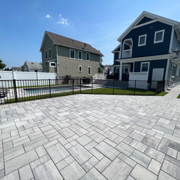 Expansive modern paver patio, black fence, swimming pool, and residential houses. | Down To Earth Landscaping | Jackson New Jersey, USA (732) 833-7702