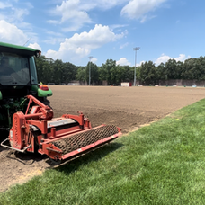 Green John Deere tractor tilling a large dirt sports field. Commercial Landscaping near me | Down To Earth Landscaping | Jackson New Jersey, USA (732) 833-7702