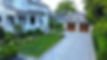 Large grey house, lush green lawn, paved driveway, two-car garage.