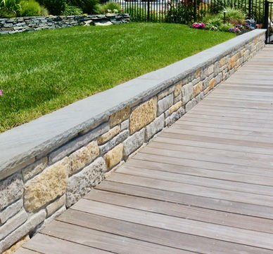 Stone retaining wall separates wooden deck from vibrant green lawn. Residential landscaping near me| Down To Earth Landscaping | Jackson New Jersey, USA (732) 833-7702